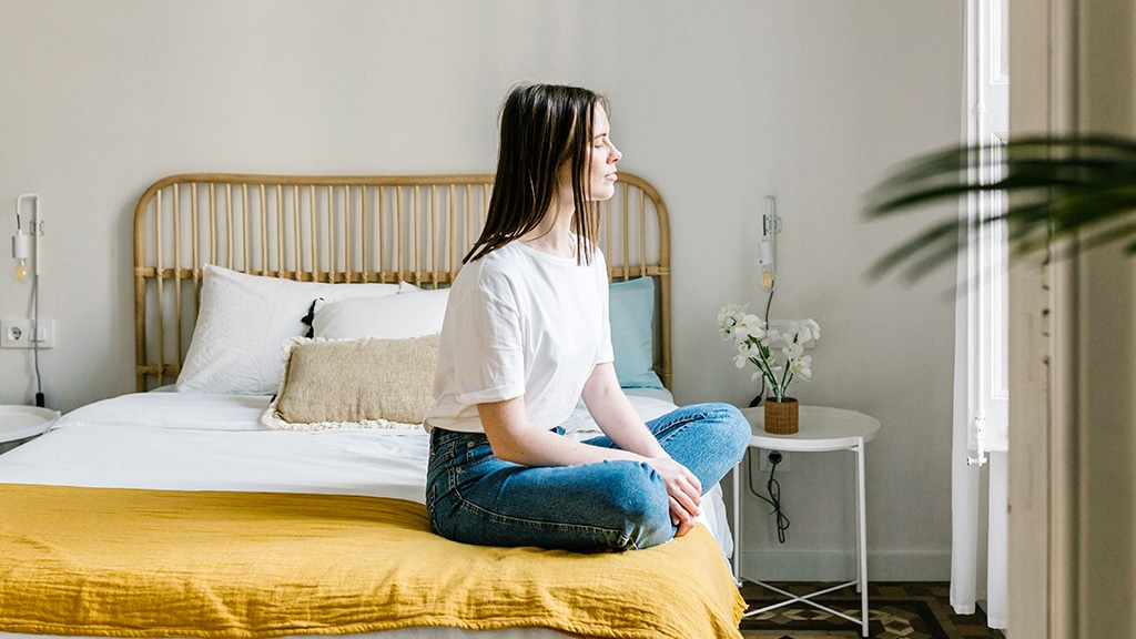 Woman sitting on the edge of her bed looking outside the window