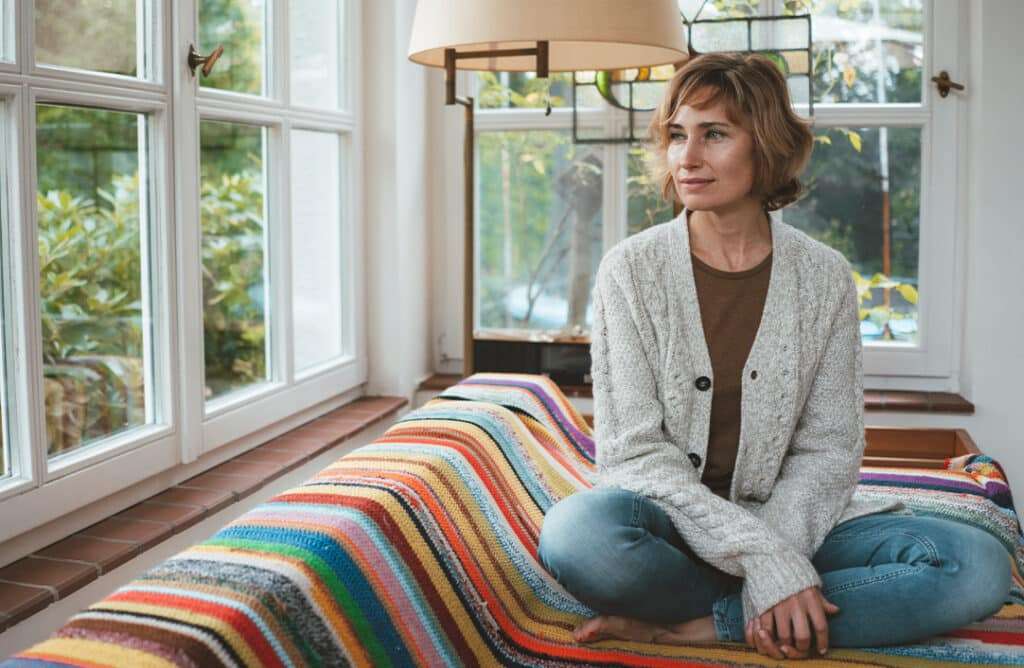 Middle aged woman sitting on couch beside window looking out