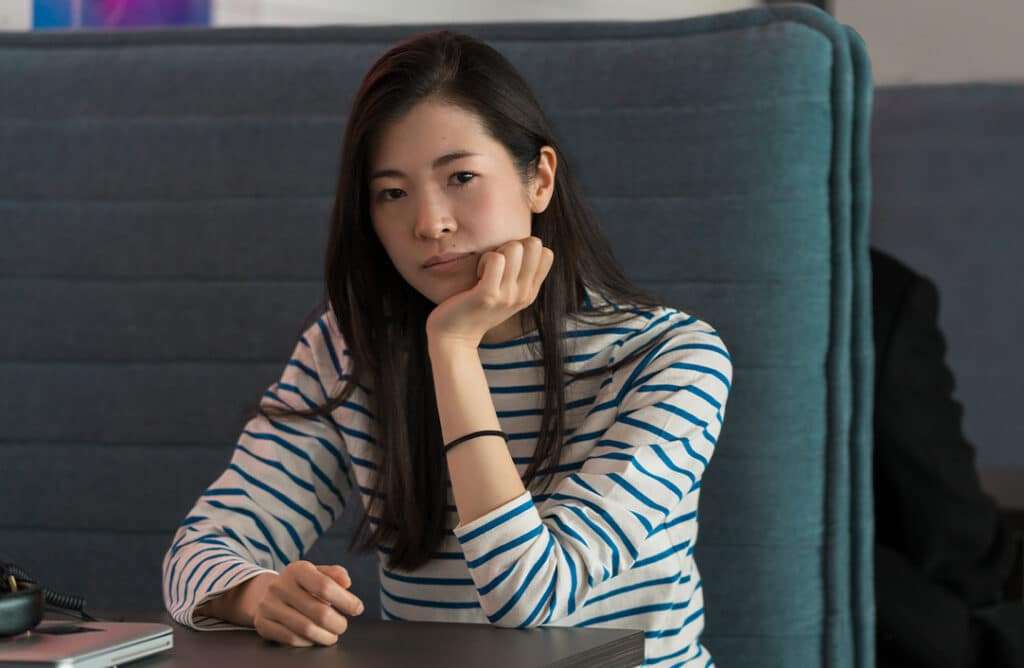 Woman sitting in booth wearing a striped shirt and looking sad.