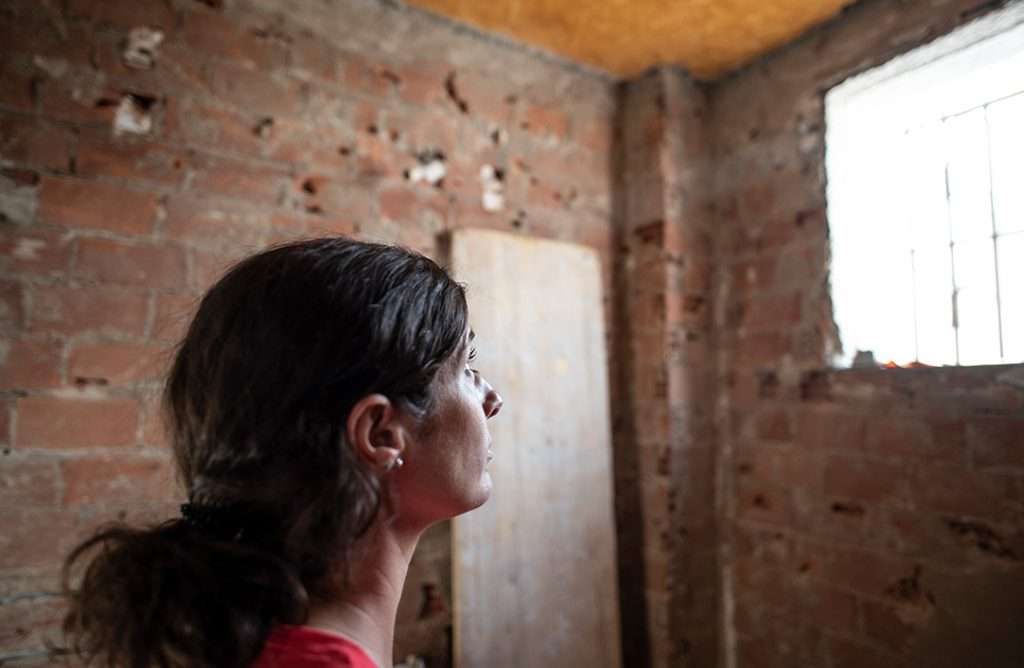 Incarcerated woman in red with hair pulled back looking out cell window.