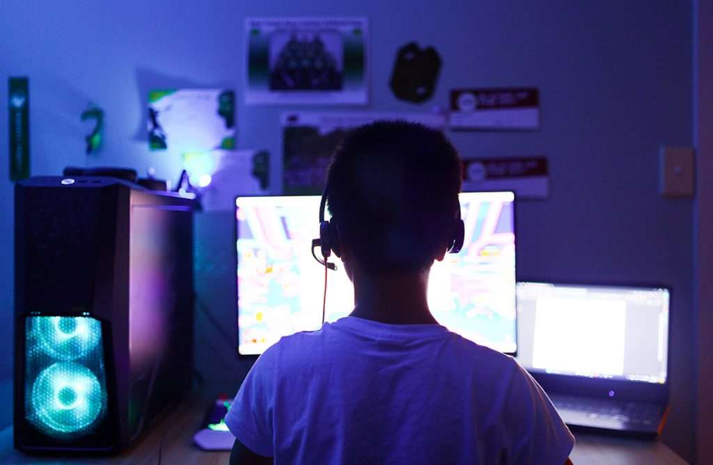 Boy with headphones on playing online computer games in dark room
