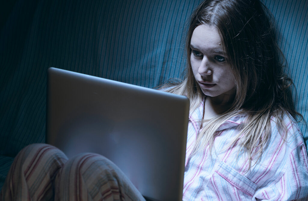 teenage girl looking at laptop screen in a dark room.
