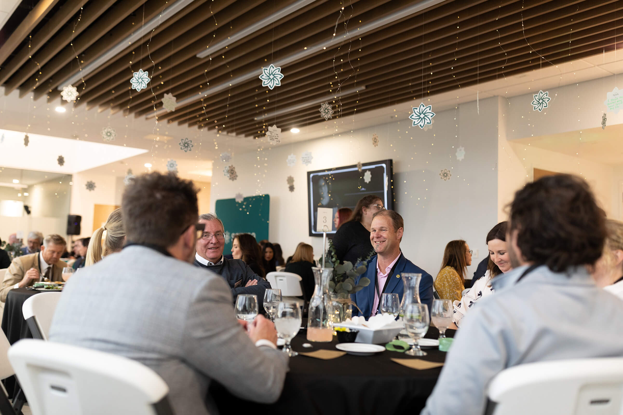 Group of individuals eating at tables with white chairs and black table cloths.