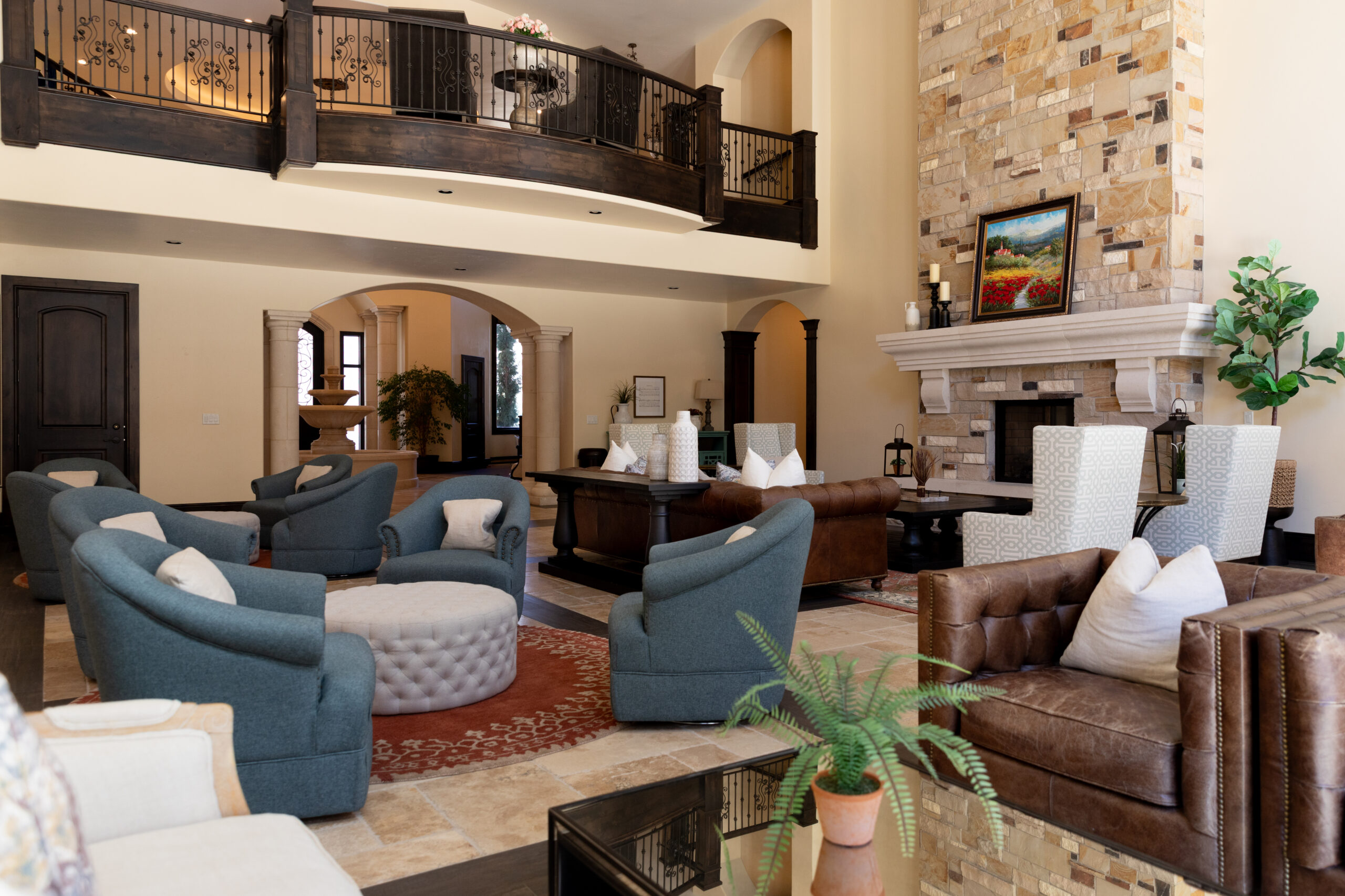 Great room with a collection of seating areas ranging from blue fabric armchairs to brown leather couches and loveseats. The are grouped together to allow areas of natural conversation to occur.