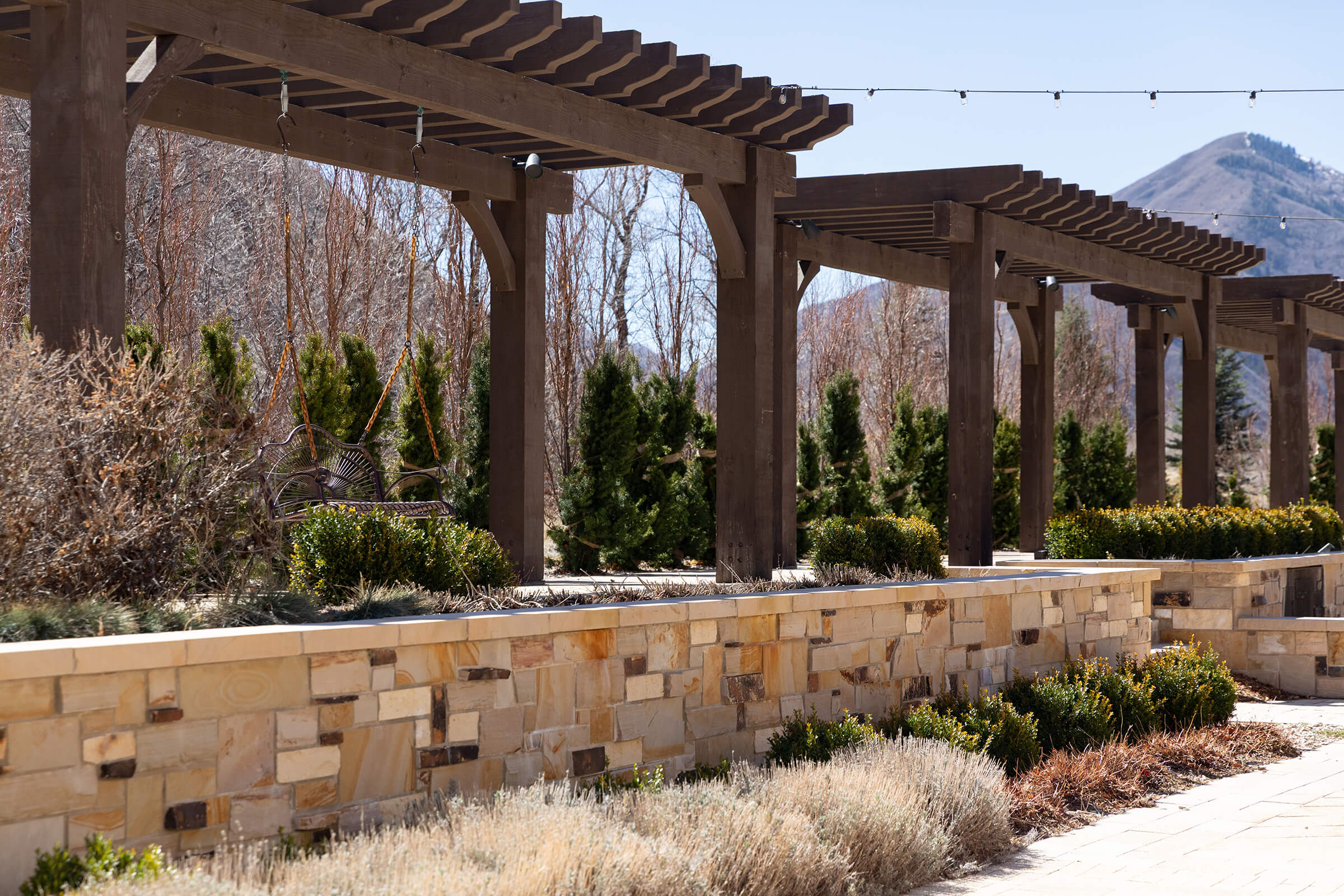 Outside scene with wooden arbors, a stone brick wall, and walkway, with mountains in the background.