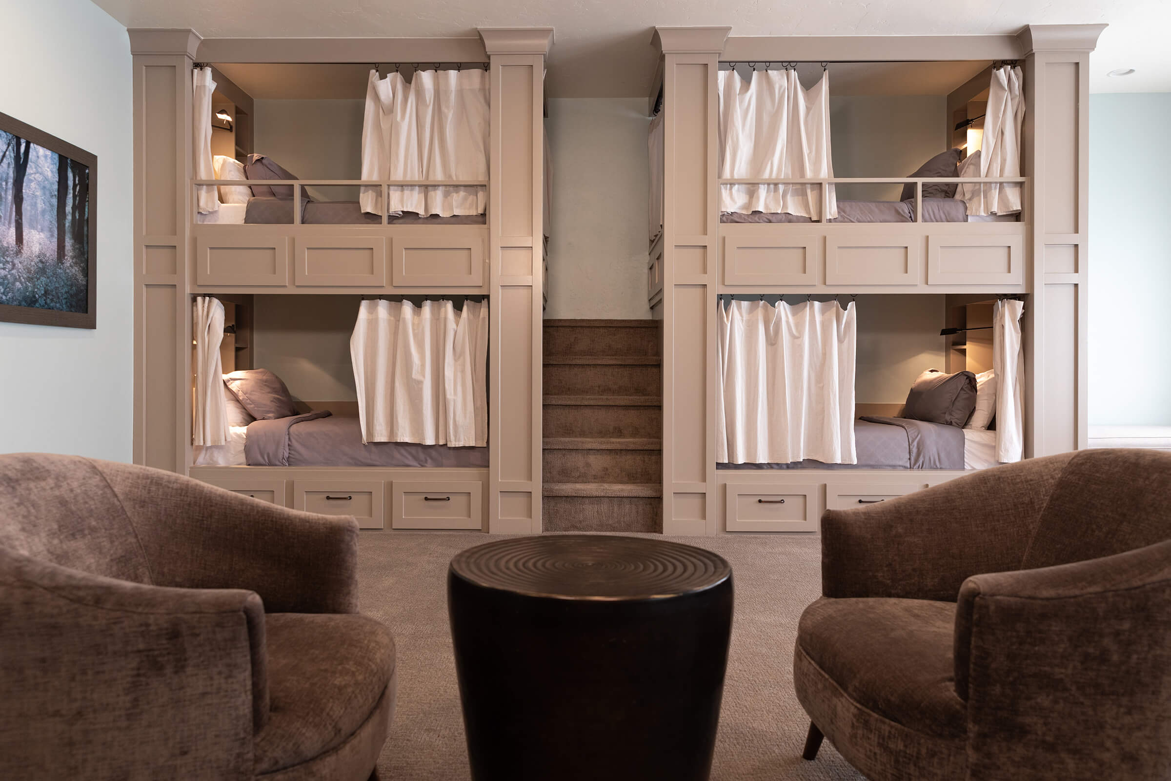 Photo of a bedroom showing four bunkbeds with privacy drapes and two armchairs with a center round table.