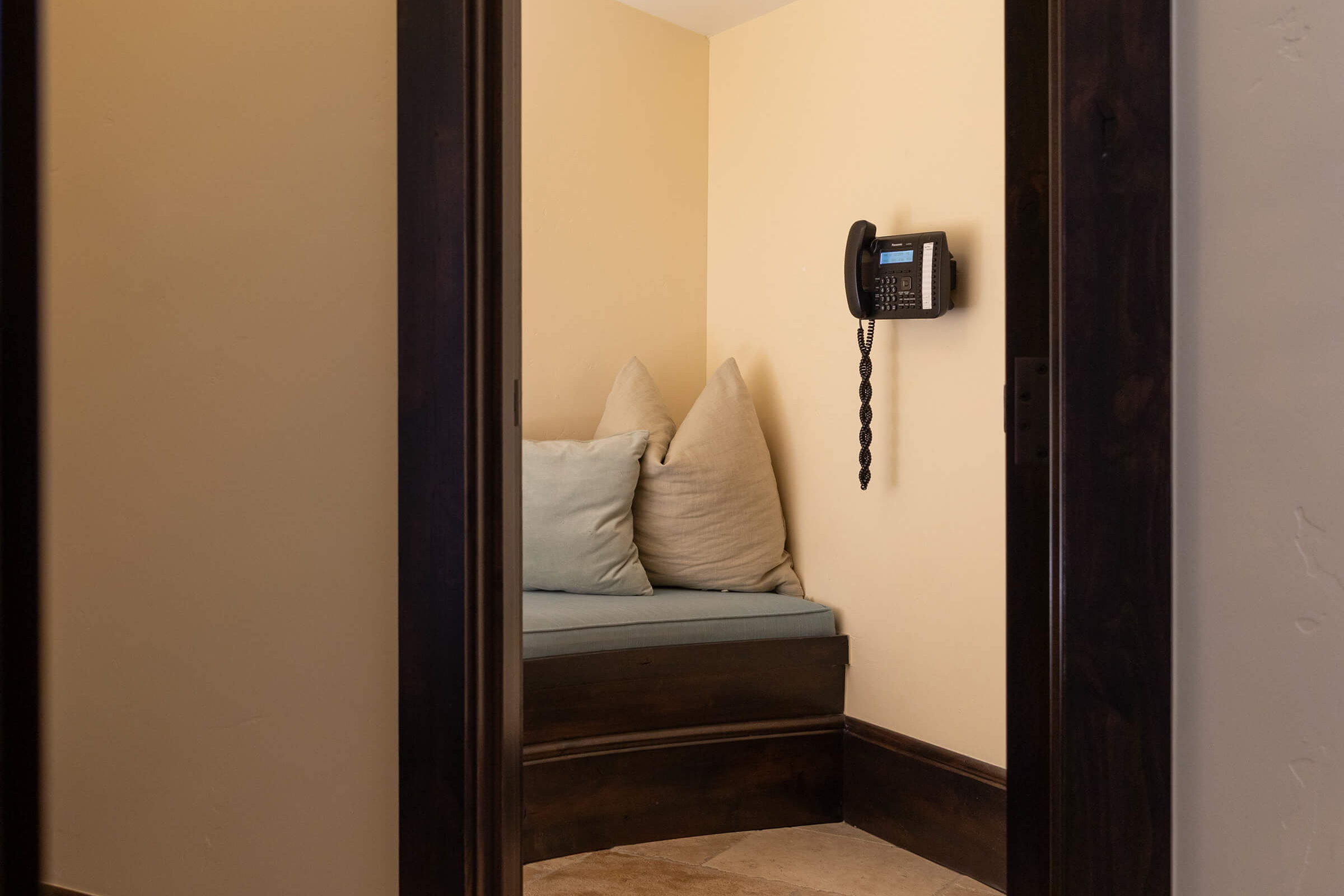 Small room with fabric window seat and pillows with a phone hanging on the wall.